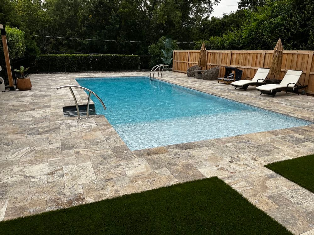 Modern outdoor pool with natural stone patio, lounge chairs, and lush greenery surrounding.