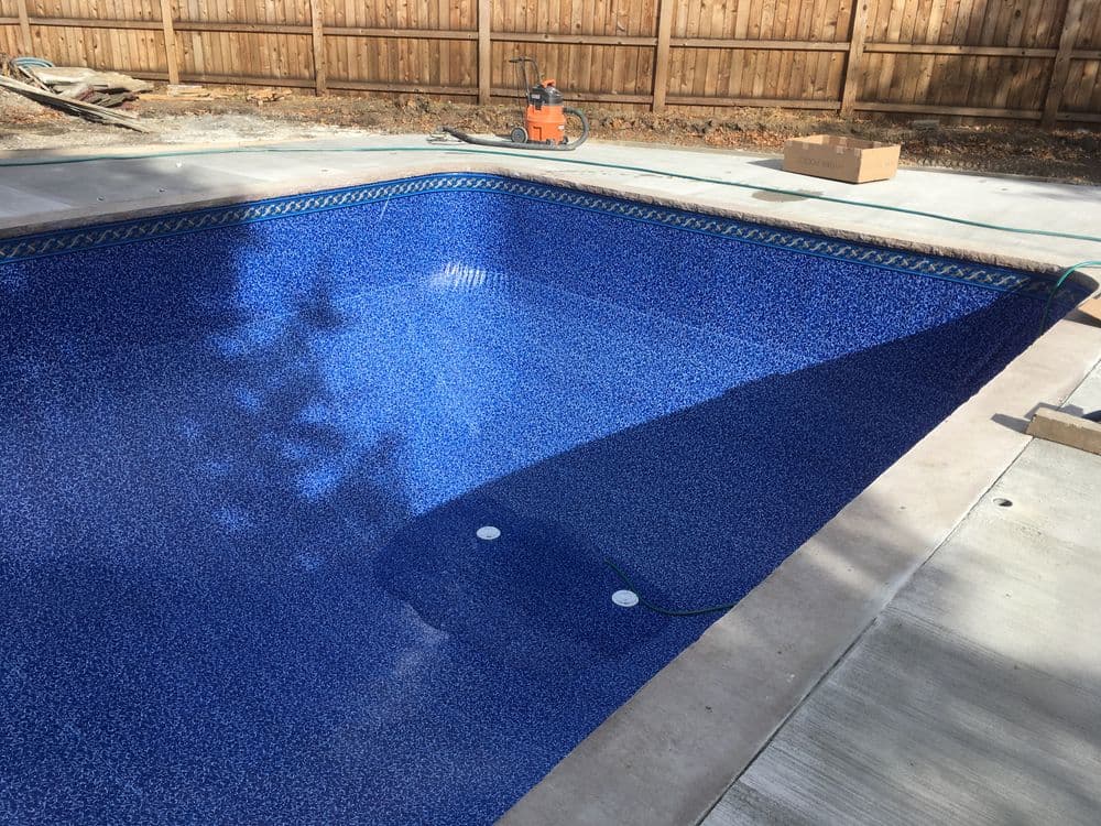 Newly constructed in-ground swimming pool with a vibrant blue interior and surrounding concrete deck.