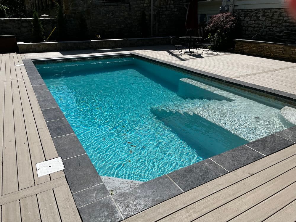In-ground swimming pool with clear water and wooden deck in a residential backyard.