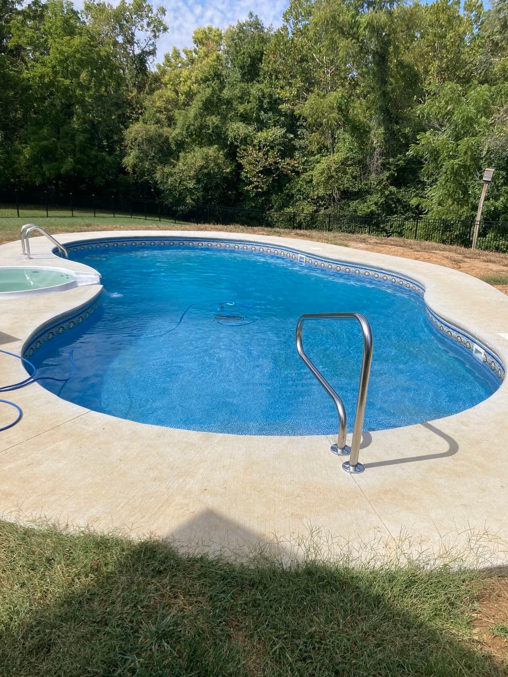 In-ground swimming pool with clear blue water surrounded by green grass and trees.