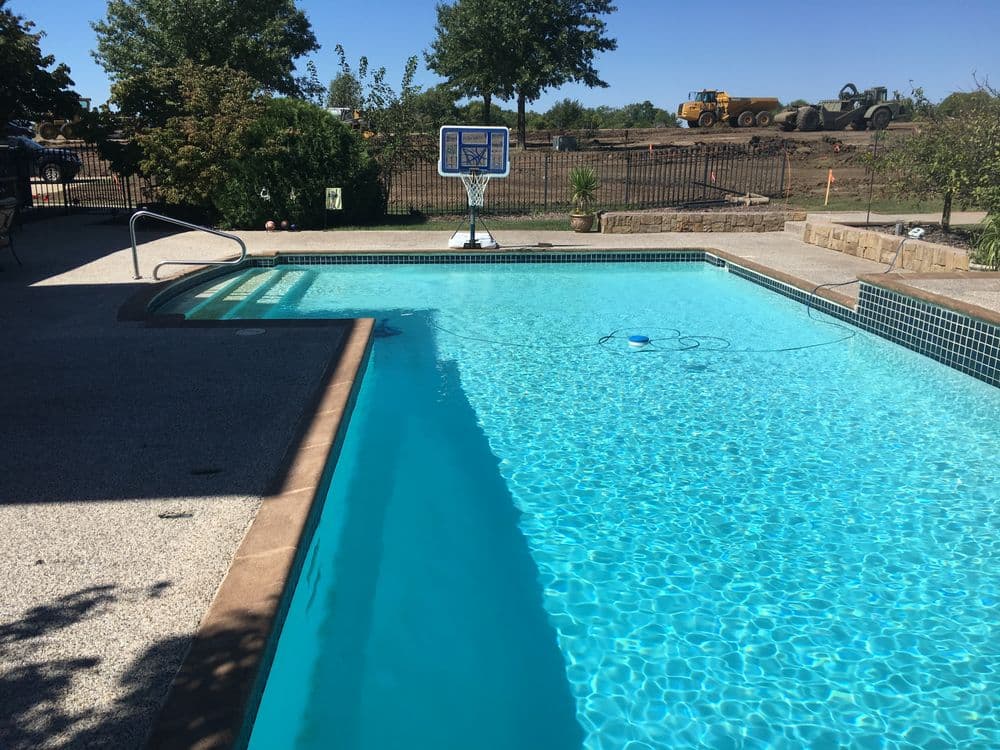 Backyard swimming pool with clear water, basketball hoop, and construction site in background.