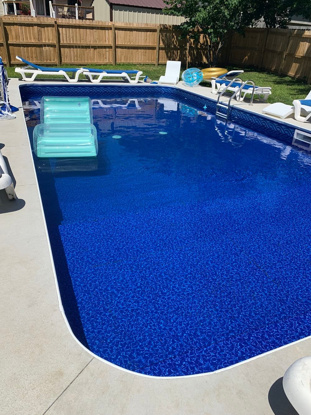 Sparkling blue swimming pool with lounge chairs and inflatable floats in a backyard setting.