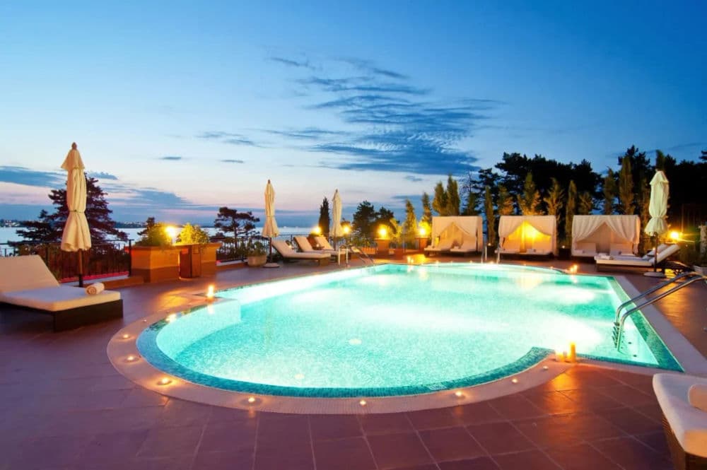 Luxury outdoor pool at sunset, surrounded by lounge chairs and umbrellas in a serene setting.