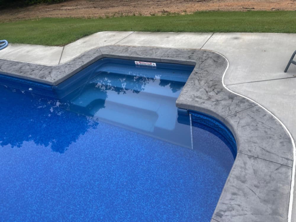 In-ground swimming pool with blue water and textured stone edging on a sunny day.