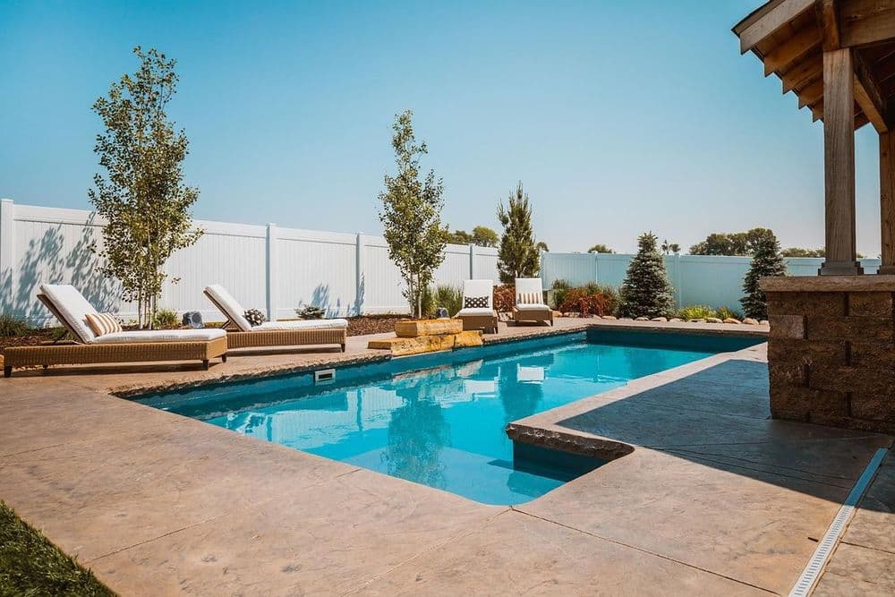 Luxury backyard oasis with a sparkling pool, lounge chairs, and landscaped greenery.