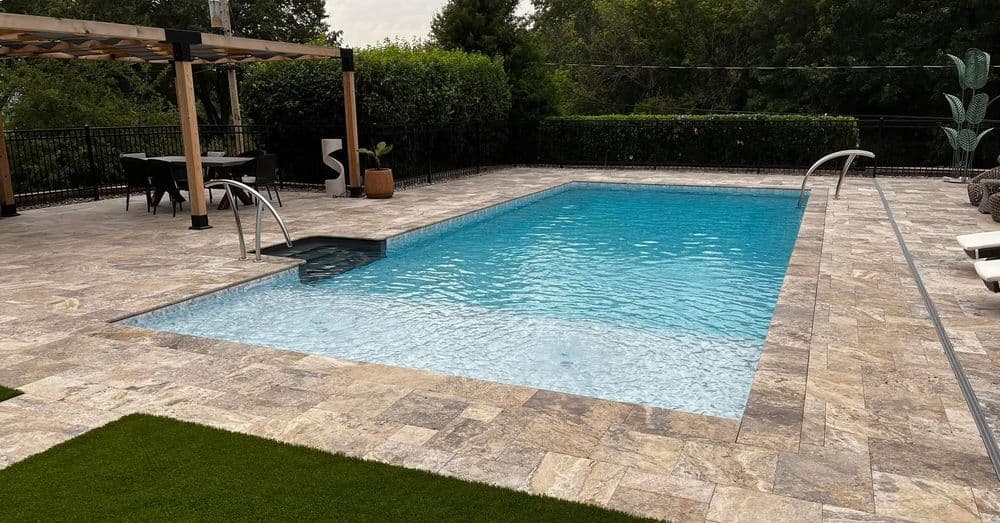 Modern backyard pool with stone deck, greenery, and seating area for relaxation.