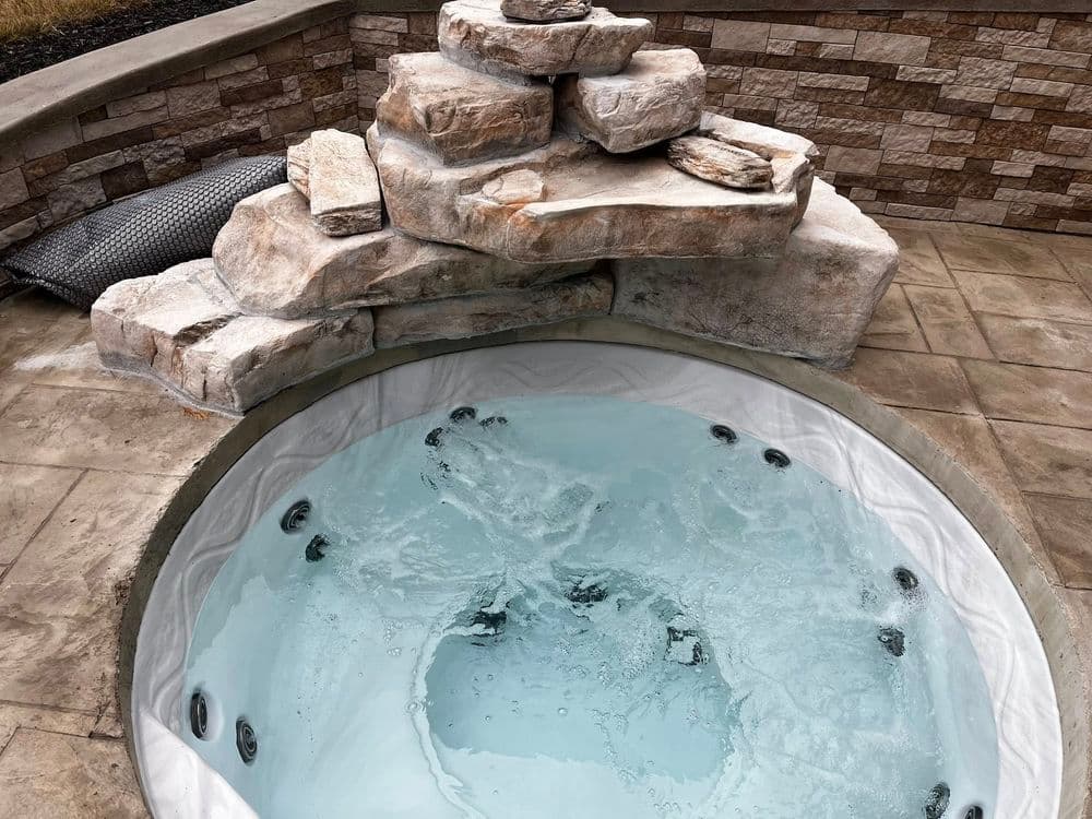 Outdoor hot tub with stone features and bubbling water, surrounded by a patio.